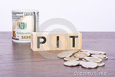 top view of wooden cubes with text PIT over US dollar banknotes and coins on a brown wooden background Stock Photo