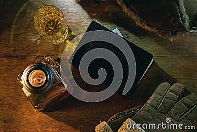 Top view of a wooden table with a black book, a bottle of bourbon, a glass and snow gloves Stock Photo