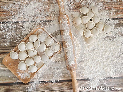 Top view on wooden table with homemade food. hand made raw dumplings on wooden dish and rolling pin covered with flour. Stock Photo