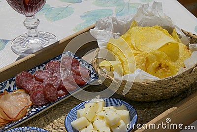 Top view of a wooden tray filled with spanish tapas with olives, cheese, smoked sausage, slices of ham and a bowl of crisps next Stock Photo