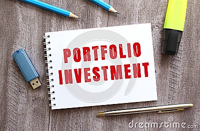 Top view of the workspace. Notepad with PORTFOLIO INVESTMENT text, pen, pencils, flash drive on gray wooden table Stock Photo