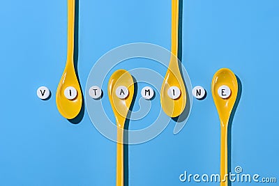 top view of yellow plastic spoons and pills with vitamine lettering in row Stock Photo