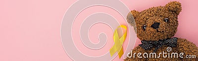 Top view of yellow ribbon and teddy bear on pink background, panoramic shot, international childhood cancer day concept. Stock Photo