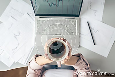 Top view. Young business woman sitting at table with cup of coffee and working on the laptop with graphics and charts Stock Photo