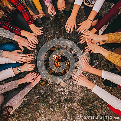 Top view of young campers sitting around and warming their hands on a campfire in the fall. Stock Photo