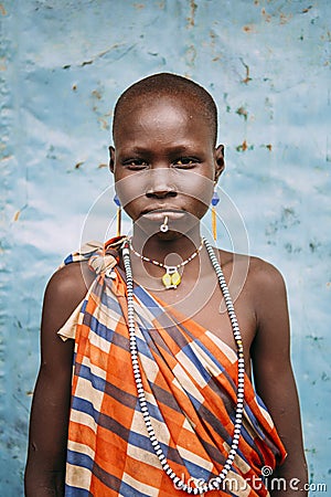 TOPOSA TRIBE, SOUTH SUDAN - MARCH 12, 2020: Girl in checkered colorful garment and with traditional accessories looking at camera Editorial Stock Photo