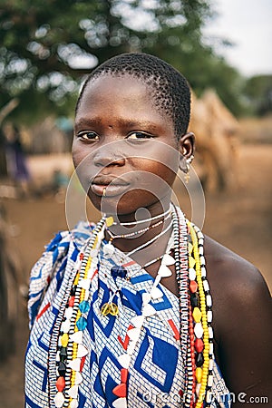 TOPOSA TRIBE, SOUTH SUDAN - MARCH 12, 2020: Teen girl in ornamental garment and with colorful accessories looking at camera on Editorial Stock Photo