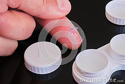 Toric contact lens on fingertip with white contact lens case and cap - composition on black reflective background Stock Photo