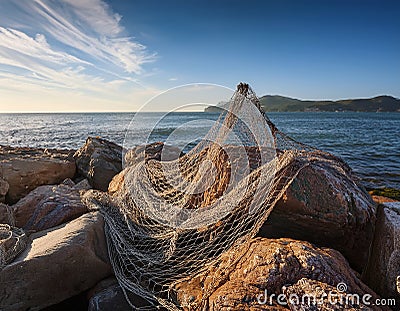 A torn net tangled around jagged rocks on a shoreline, representing entrapment and failed attempts Stock Photo