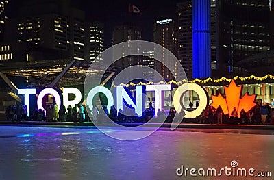 TORONTO, CANADA - 2018-01-01: People in front of TORONTO sign with Christmas tree in the night viewed across the skating Editorial Stock Photo
