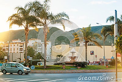 TORREMOLINOS, SPAIN - FEBRUARY 13, 2014: A crossroad with a fountain, palms and flower beds and mountains at the background and Editorial Stock Photo