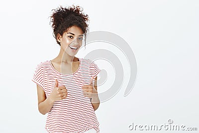 Totally agree with your opinion. Satisfied happy and outgoing woman with dark skin in striped t-shirt, raising thumbs up Stock Photo