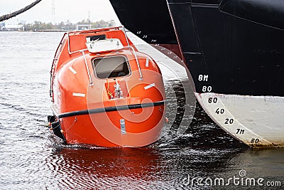 Totally Enclosed Lifeboat floating near big vessel Stock Photo