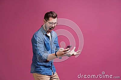 Always in touch. Smiling young man holding smart phone and looking at it. Portrait of a happy man using mobile phone Stock Photo