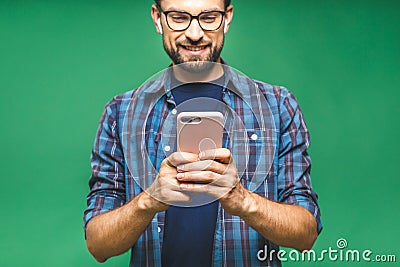 Always in touch. Smiling young man holding smart phone and looking at it. Portrait of a happy man using mobile phone isolated over Stock Photo