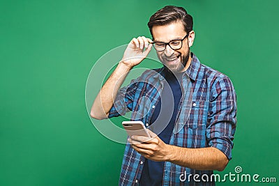 Always in touch. Smiling young man holding smart phone and looking at it. Portrait of a happy man using mobile phone isolated over Stock Photo