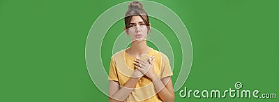 Touched and pleased attractive young woman in yellow t-shirt holding palms pressed to chest in thankful and grateful Stock Photo