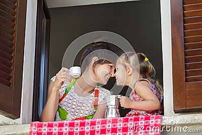 Touching with noses mother and her two years old daughter holding traditional Italian coffee set of white cup and metal Stock Photo