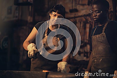 The toughest metal withstands the strongest fire. Shot of a young woman hitting a hot metal rod with a hammer in a Stock Photo