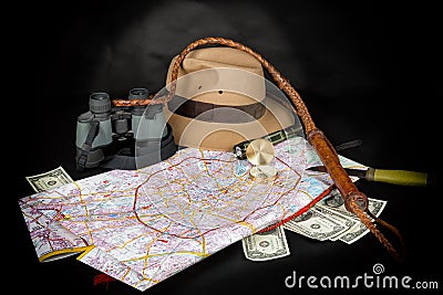 Tourism and adventure concept. Compass on city map with flashlight, fedora hat, bullwhip, binocular, knife and dollar bills on dar Stock Photo