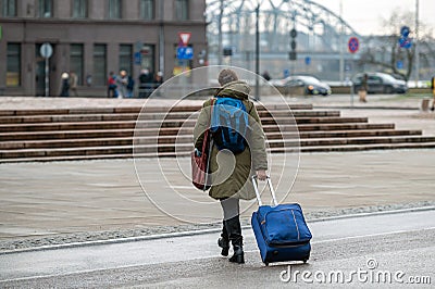 A tourist with a backpack pulls a suitcase on wheels down the street, rear view, Riga, Latvia Editorial Stock Photo
