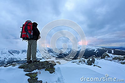 A tourist with a backpack stands on a gray stone. Stock Photo