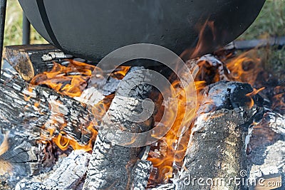Tourist black cauldron with food on bonfire, cooking in the hike. Preparation of pilaf or soup on fire Stock Photo
