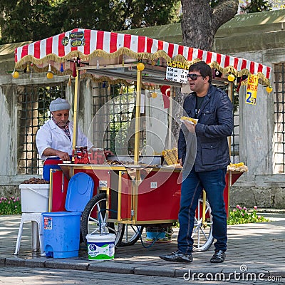 Tourist buying food from a traditional Turkish chestnut and corn cart in Sultan Ahmed Square, Istanbul, Turkey Editorial Stock Photo