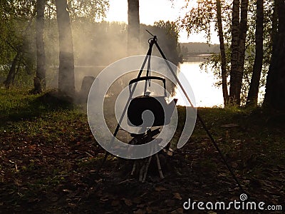 Tourist camping kettle on the fire boils on the background of the forest and the river Stock Photo