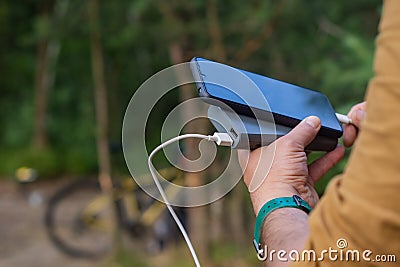 A tourist charges a smartphone with a power bank on the background of a bicycle in forest Stock Photo