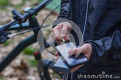 A tourist charges a smartphone with a power bank on the background of a bicycle in nature Stock Photo