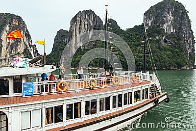 Tourist cruising boat over the emerald water with towering limestone islands that have growing green trees on it in summer. Editorial Stock Photo