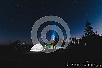 Tourist with flashlight near his camp tent at night Stock Photo