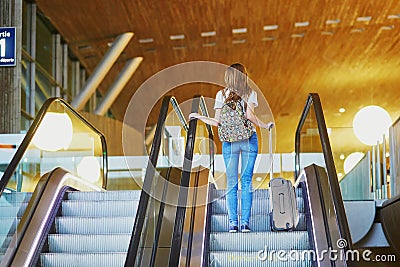 Tourist girl with backpack and carry on luggage in international airport, on escalator Stock Photo