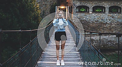 Tourist girl look at the camera walking old historical city and hold in hands retro camera, young woman stands on suspension Stock Photo
