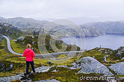 Tourist girl looks at the lake and the narrow road in the mountains at foggy cloudy weather in summer Stock Photo