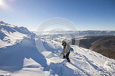 Tourist hiker climber in winter clothing with backpack climbing dangerous rocky steep mountain slope covered with deep snow, white Stock Photo