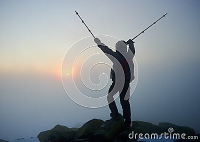 Tourist hiker man with backpack on rocky mountain on misty blue sky and raising sun background. Stock Photo