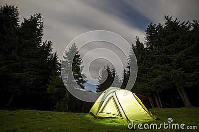 Summer camping at night. Illuminated tourist tent on green clearing on distant mountain background Stock Photo