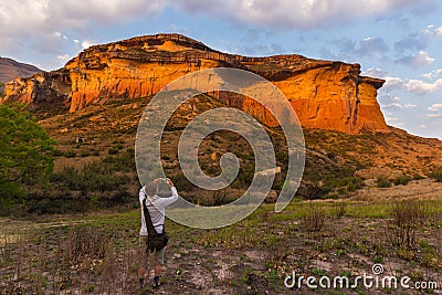 Tourist holding smart phone and taking photo at scenic cliff illuminated by sunset light in the majestic Golden Gate Highlands Nat Stock Photo