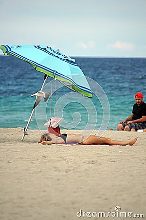 Tourist lying under a colorful beach umbrella on Dania Beach Editorial Stock Photo