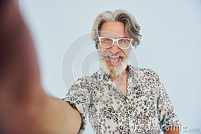 Tourist makes selfie. Senior stylish modern man with grey hair and beard indoors Stock Photo