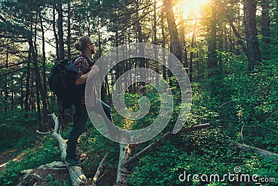 Tourist man with backpack walks through the forest and enjoys the view of the sun Stock Photo