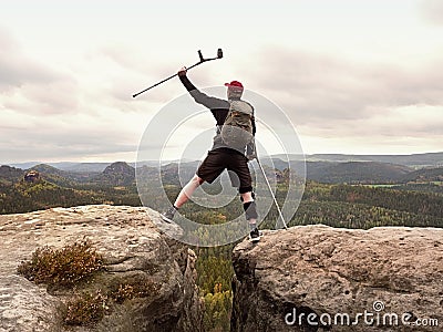 Tourist with medicine crutch above head achieved mountain peak. Hiker with broken leg Stock Photo