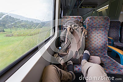 Tourist riding train feet on seat, backpack, rainy weather. Stock Photo