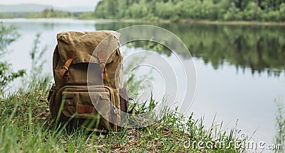 Tourist`s brown backpack on the shore of a river. A great trip to nature in a dense green forest with a reservoir Stock Photo