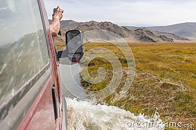 Tourist`s hand leaned out of the car window, photograph the view. Journey of river on SUV car. Mongolia - Altai. photo made from Stock Photo