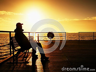 Tourist sit on wharf bench and enjoy misty sunny morning at sea. Smooth water Stock Photo