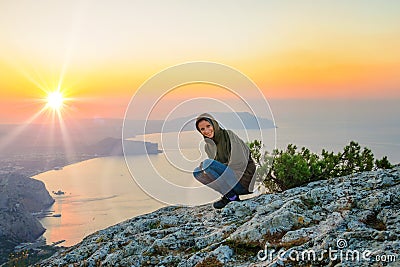 A tourist sits on a cliff overlooking the sea , watching the sun rise, travel concept Stock Photo