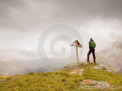 Tourist stand on rocky view point and watching into misty Alpine valley. Wooden cross at a mountain peak Stock Photo